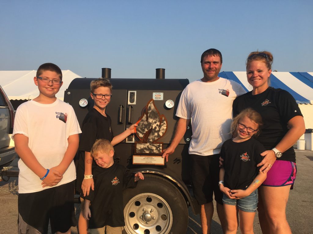 A family proudly displaying their award from a BBQ competition featuring the ABS Judge.