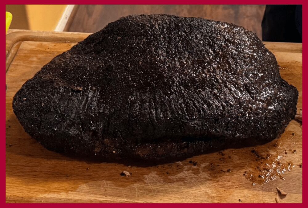 A whole smoked brisket with a heavy black pepper and coriander pastrami rub, showing a professional dark bark on an American Barbecue Systems smoker.